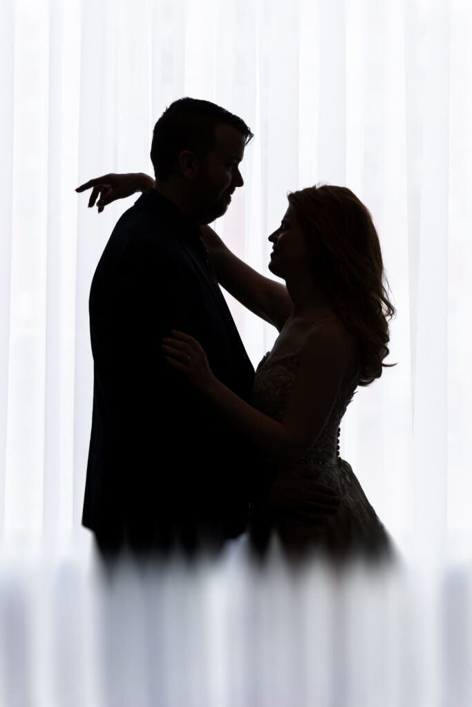 Silhouette of a couple slow dancing face to face, backlit by sheer white curtains