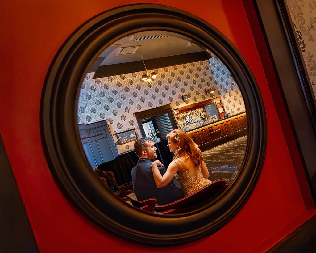 Couple sharing a close moment reflected in a round mirror inside a warmly lit vintage bar