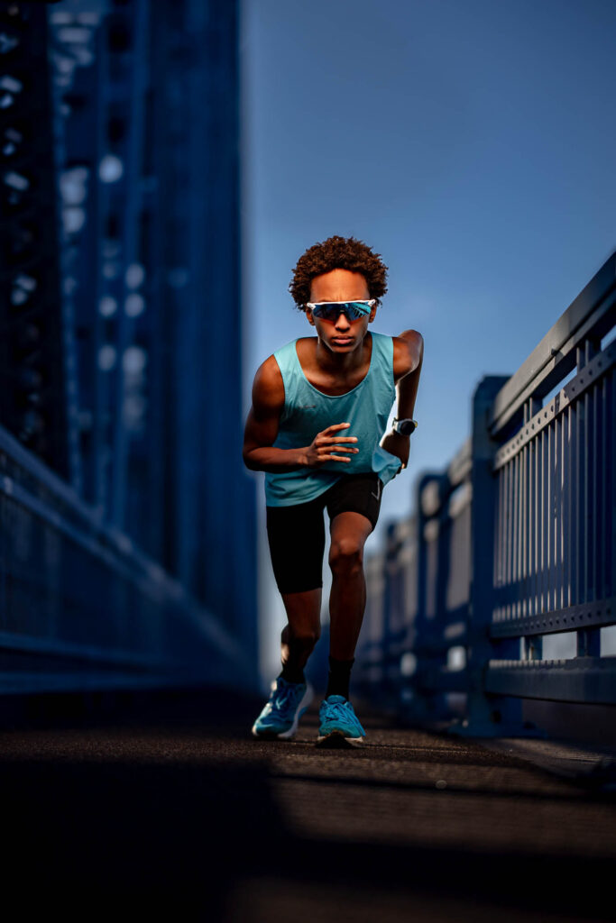 Teen male senior track athlete sprinting full speed down Cass Street Bridge corridor in La Crosse WI, flash-lit against…