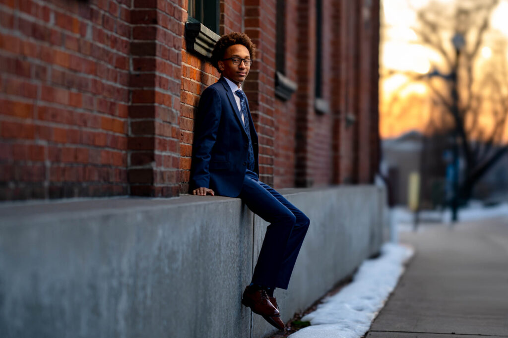 Teen male senior with glasses glancing back over shoulder with a smirk, arms pointed outward, vivid mural backdrop