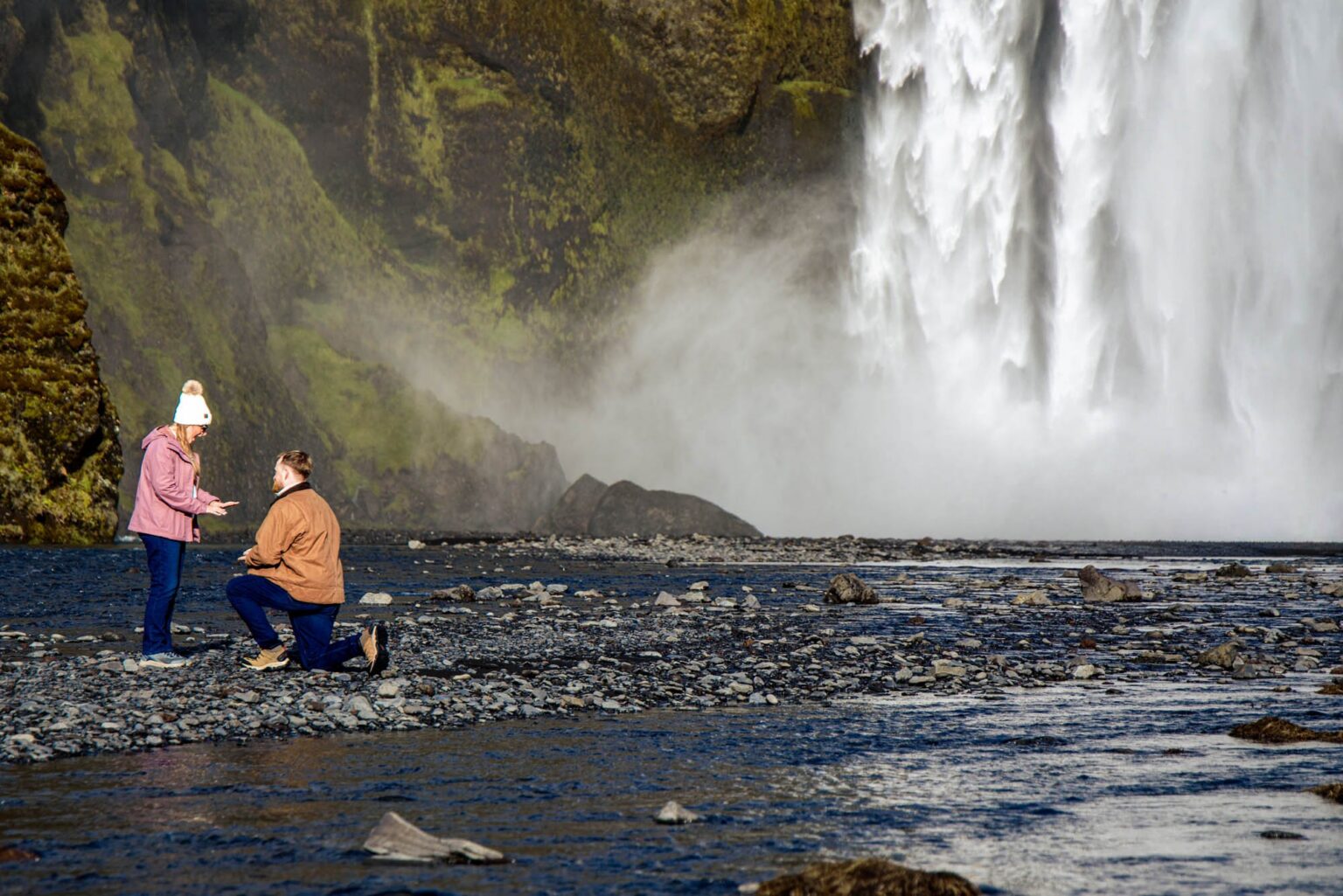 A man on one knee proposing at the foot of Skogafoss waterfall, Iceland