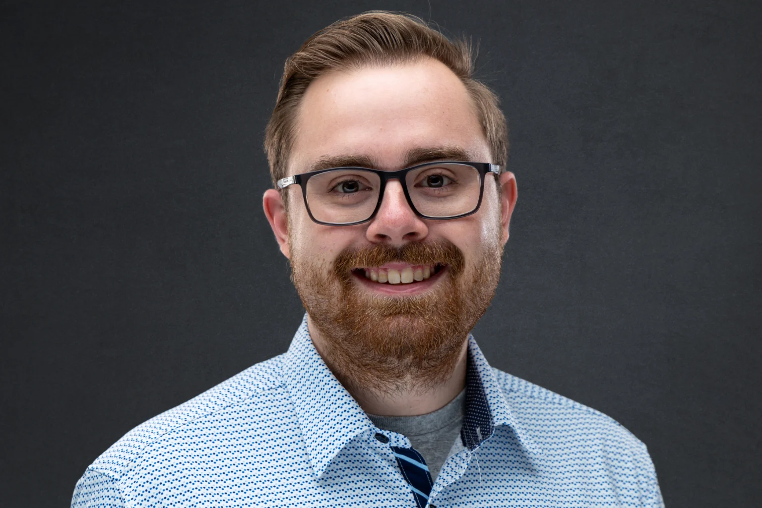 Studio headshot of a man in glasses against a grey background