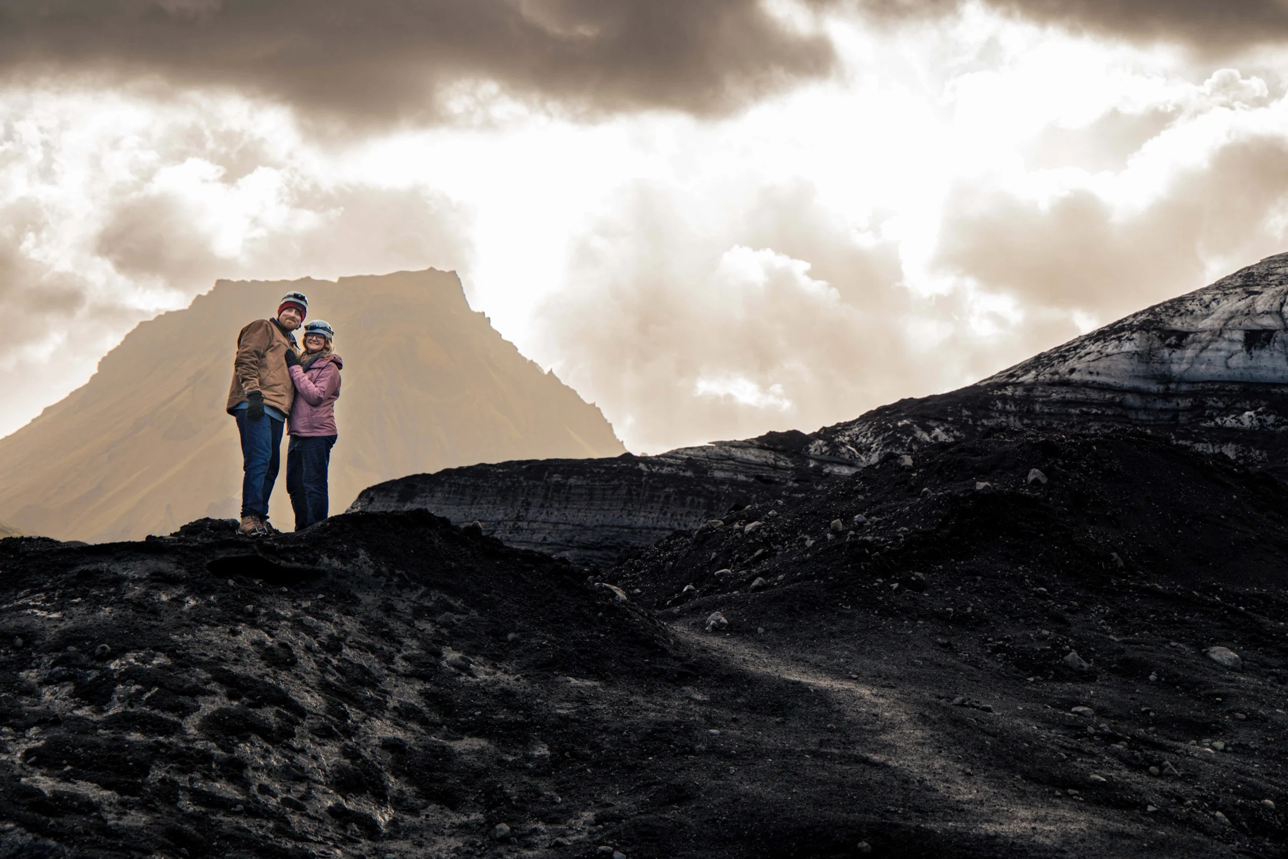 Couple standing together on black volcanic rock with layered mountains behind them