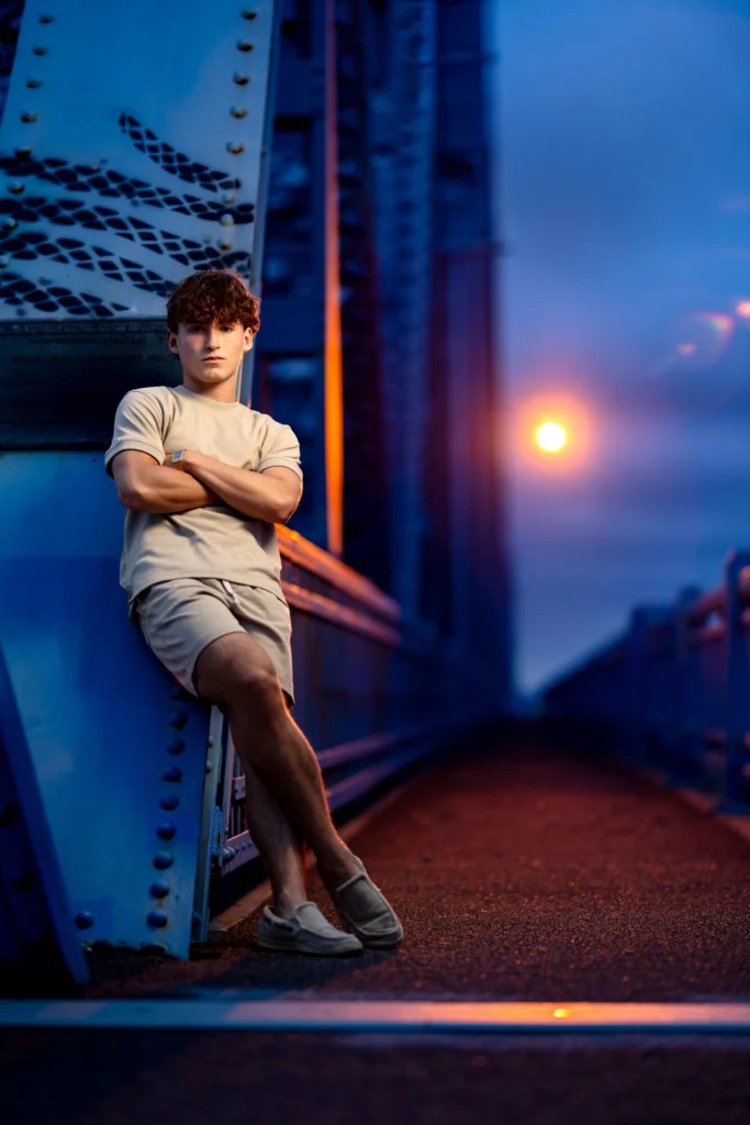 Full-length senior portrait on Cass Street Bridge at blue hour, warm bridge lamp glowing in background, La Crosse WI