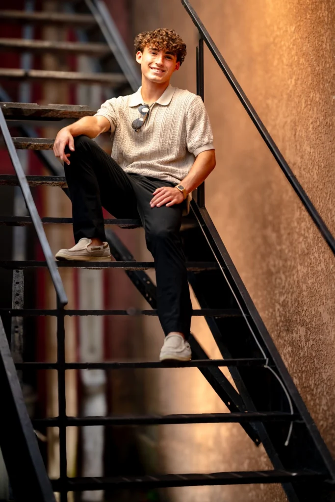 High school senior laughing genuinely on black iron fire escape stairs, warm stucco wall, La Crosse Wisconsin