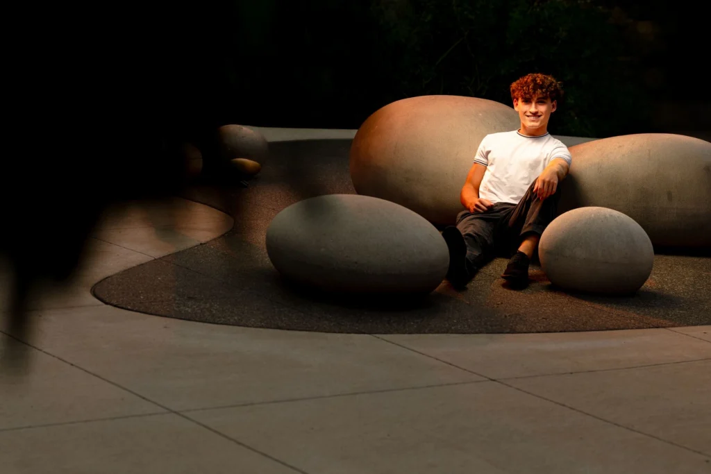 High school senior laughing naturally while seated among large stone sculptures, warm dramatic light, La Crosse, Wisconsin