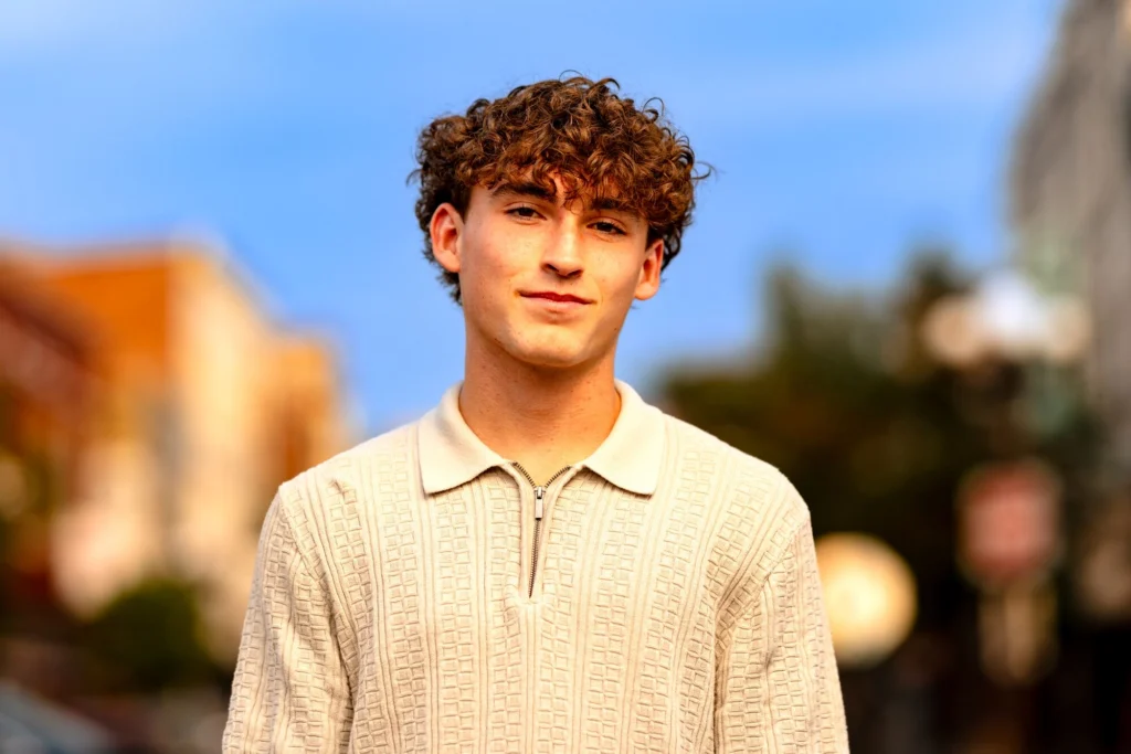 Close-up senior portrait of a curly-haired person glowing in warm golden light on a downtown La Crosse street