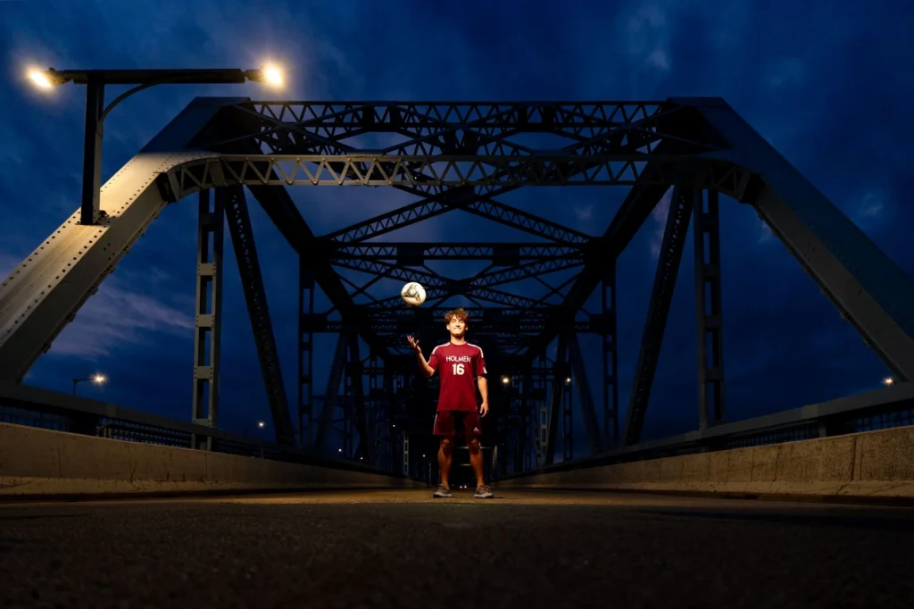 Senior spinning a soccer ball under the arch of the Cass Street Bridge at night