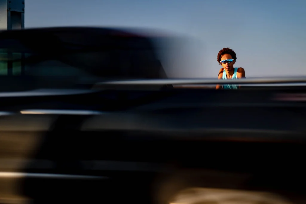 Senior in blue sunglasses framed by passing traffic on the Cass Street Bridge