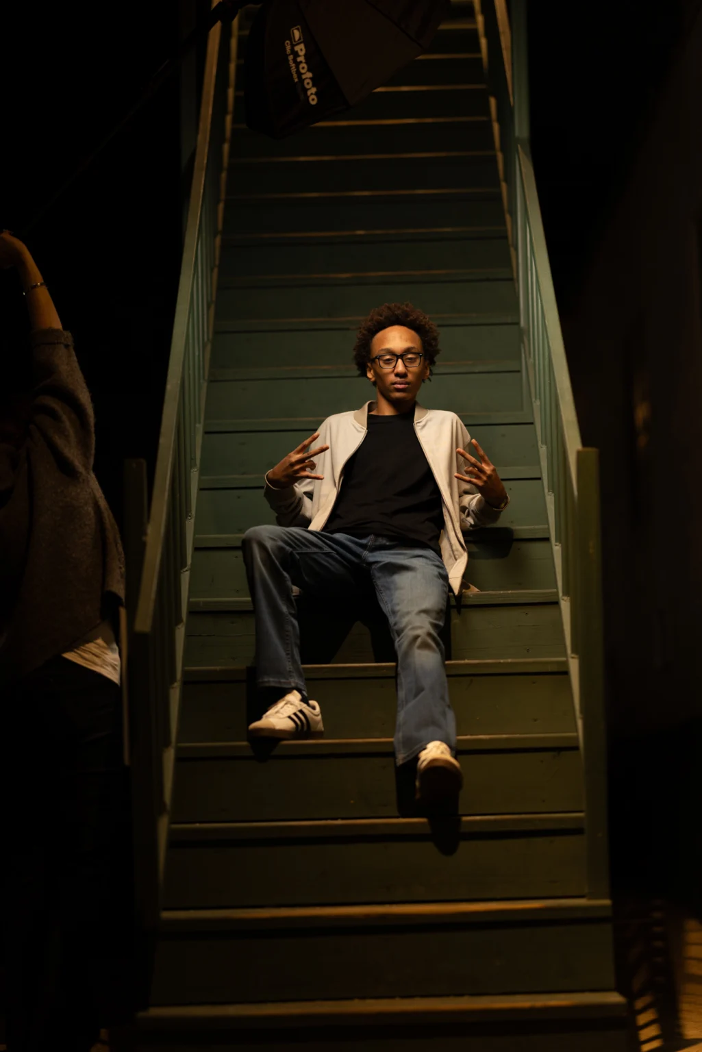 High school senior in glasses and a blazer seated on a dark staircase under built light, La Crosse