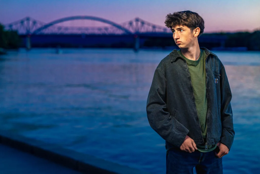High school senior on the Mississippi River at dusk with the Cass Street Bridge behind him, La Crosse, Wisconsin